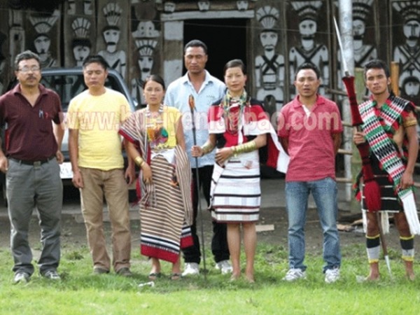 Project officials along with villagers in front of a traditional Maram house